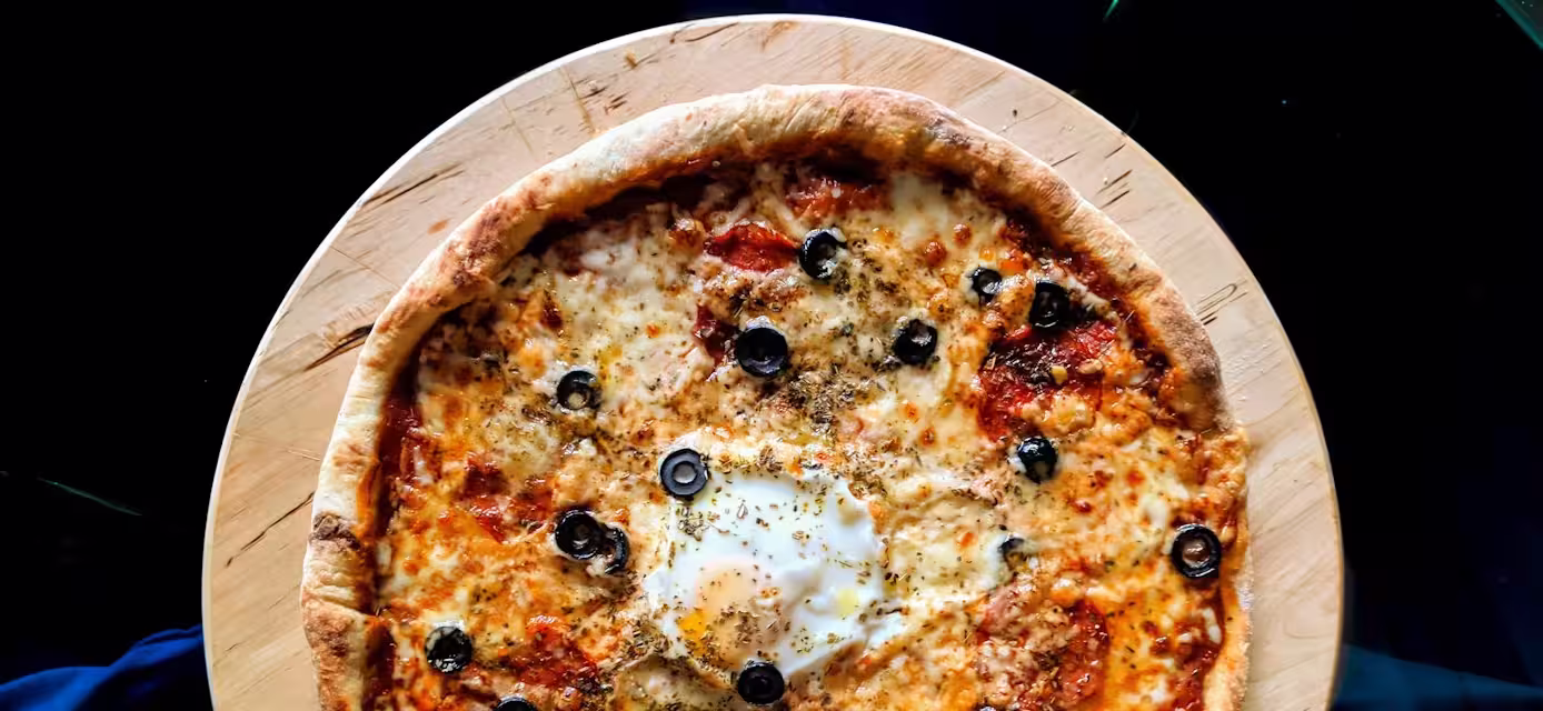 Baked pizza with tomatoes, cheese, olives, salami, and a fried egg