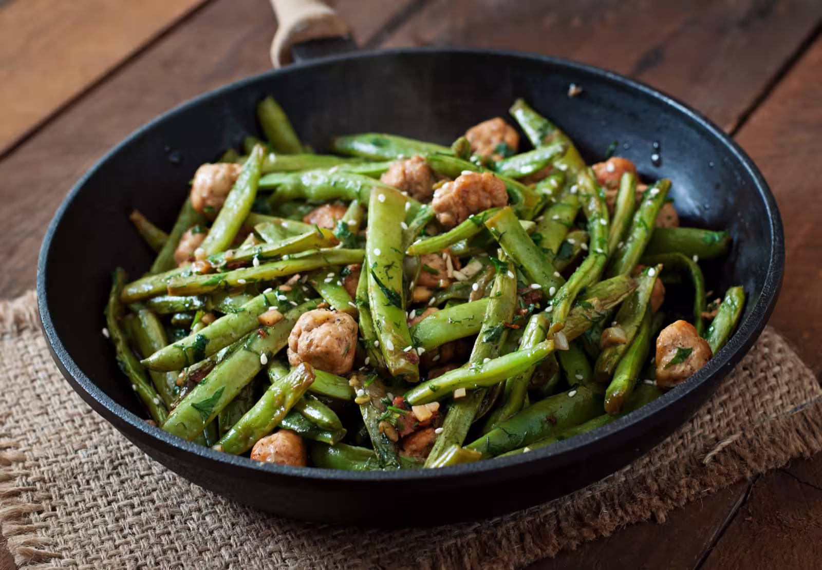 A plate of Asian-style green beans fried with chicken meatballs and garlic, garnished with sesame seeds