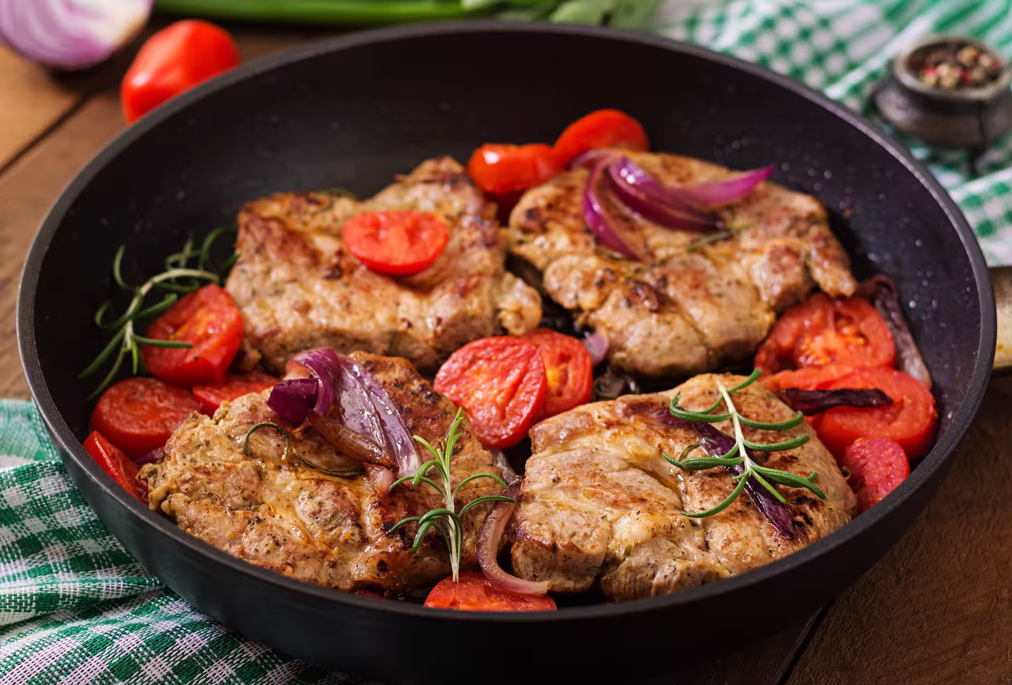 A sizzling pork steak with rosemary and tomatoes in a pan
