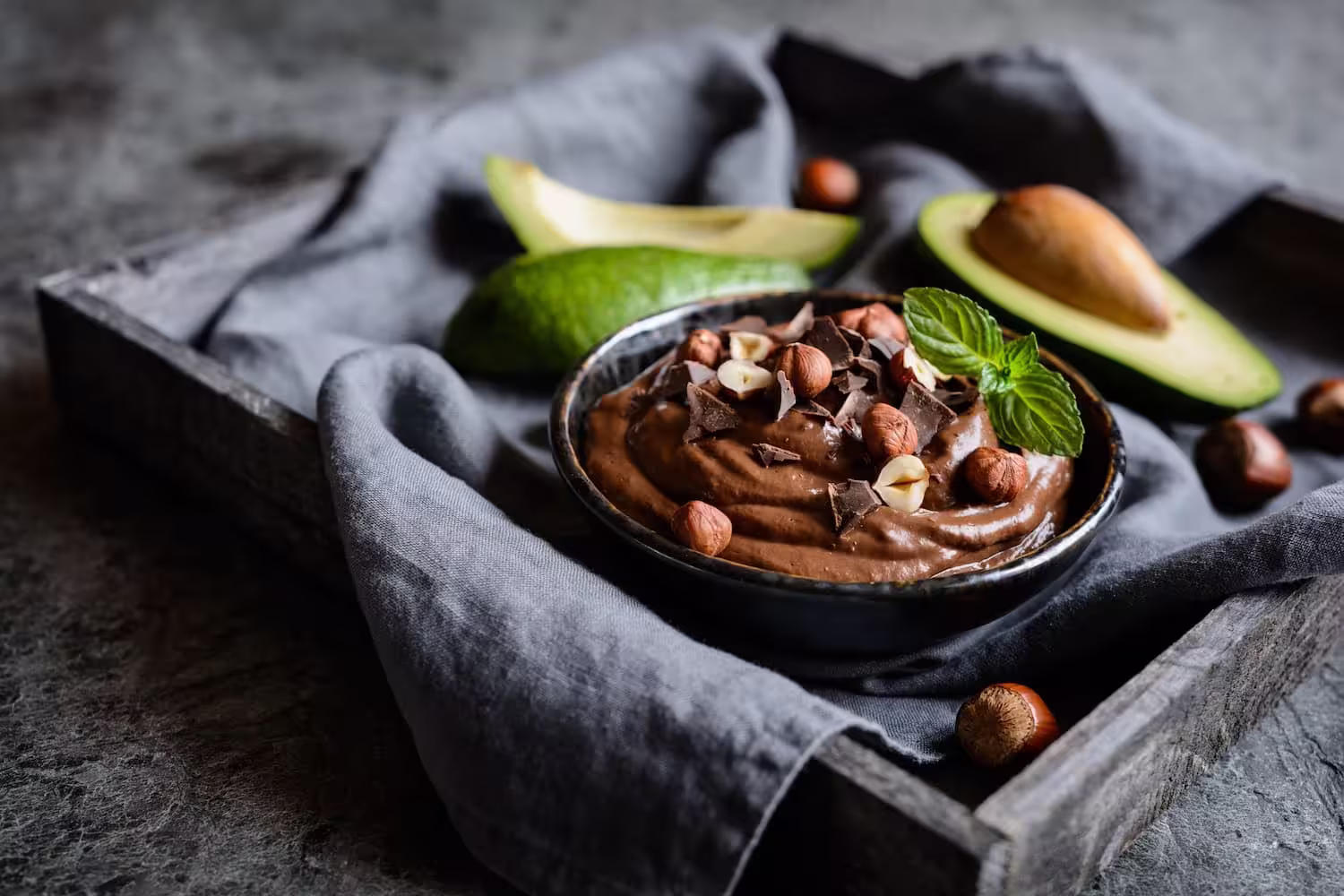 A glass of creamy avocado chocolate mousse topped with crushed hazelnuts